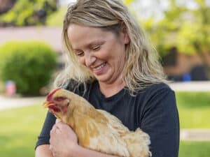 woman smiling and holding a hen and petting his neck feathers
